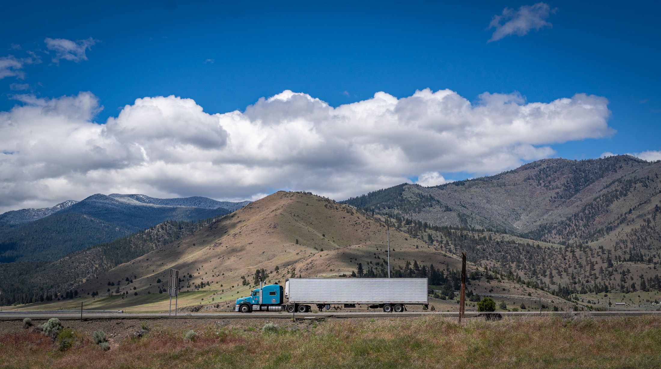 Blue semi truck and silver trailer traveling through a mountain landscape